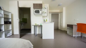 Habitación de hotel compacta con una cama, una kitchenette pequeña, un escritorio y una silla.