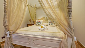 A four-poster canopy bed with a quilted mattress, floral pillows, and a bedside table with a lamp.