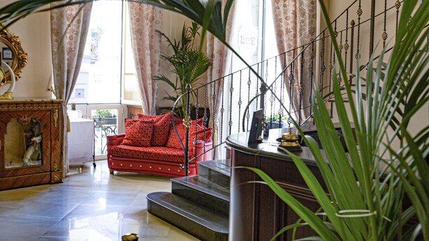 A spacious living room with a red sofa, a staircase, and a large plant.