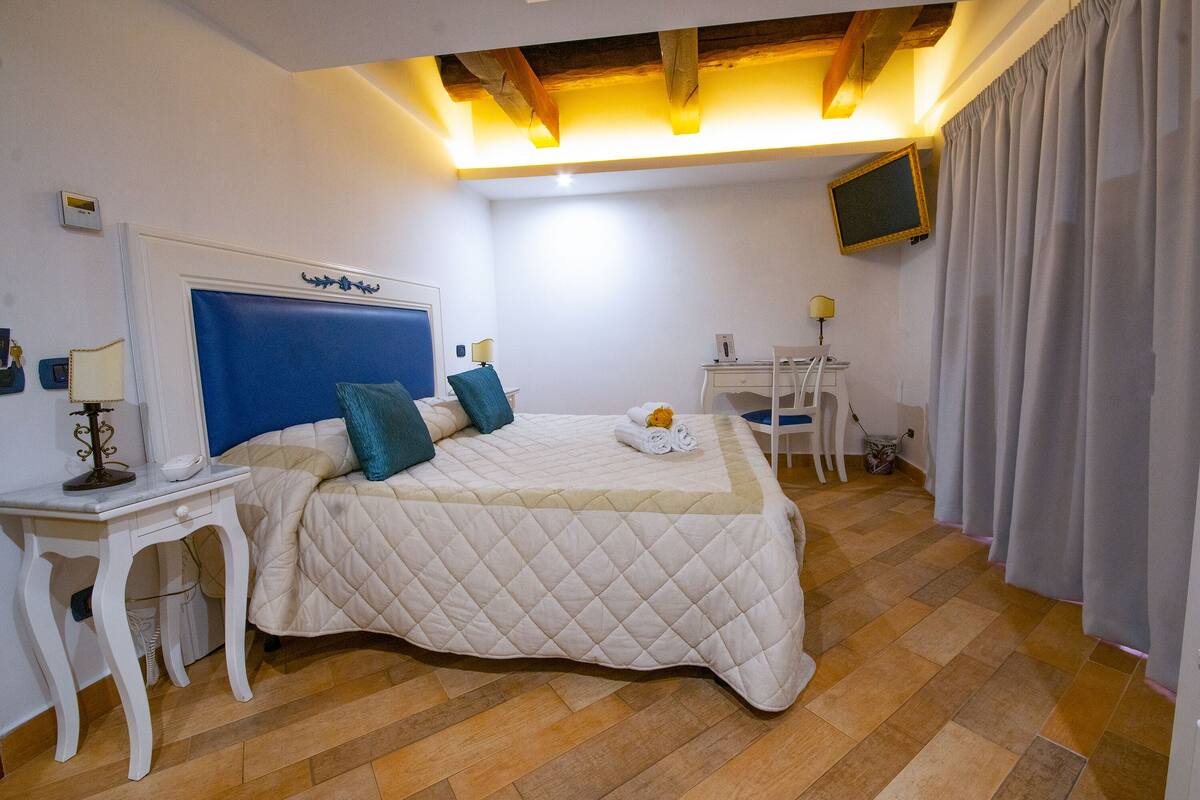 A bedroom with a bed, bedside tables, a desk, a chair, a television, and a window with curtains.