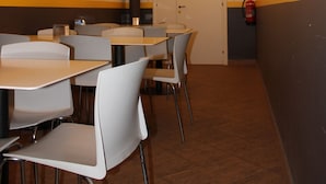 Un restaurante con mesas y sillas blancas, techo de ladrillo y un extintor en la pared.