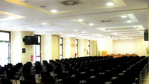 Un salón de conferencias con filas de sillas, un escenario y una pantalla grande.