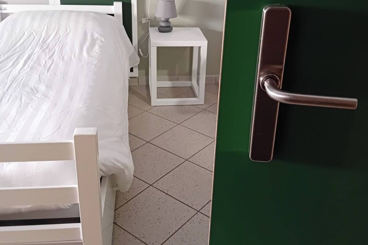 Una habitación con una cama, una mesita de noche, una lámpara y una puerta verde.