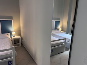 A hotel room with two single beds, each with a nightstand and a lamp. The room has a tiled floor and white walls. - Roma Scout Center - Hostel (Rome)