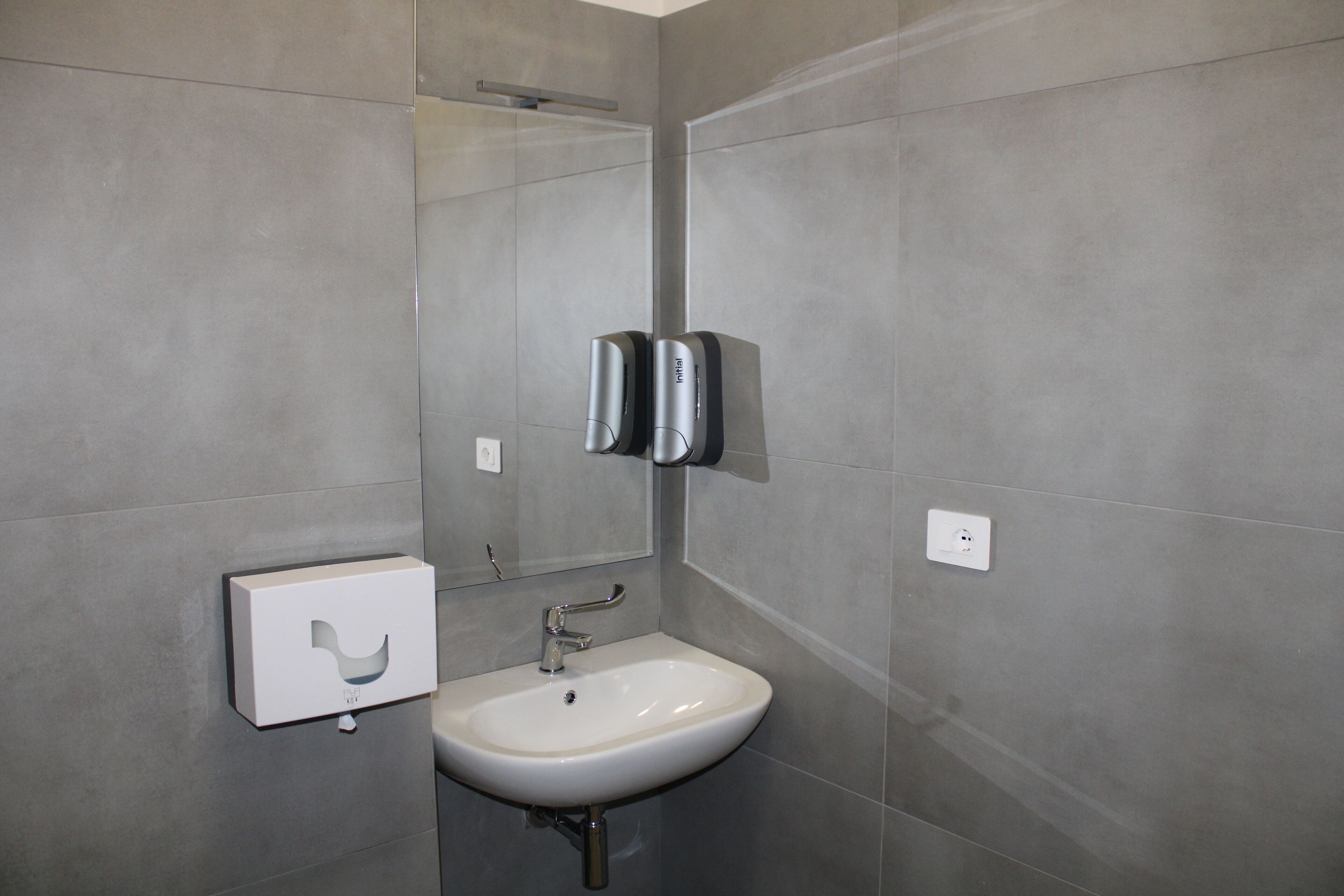 A modern bathroom with a white sink, a mirror, and two paper towel dispensers mounted on the wall.