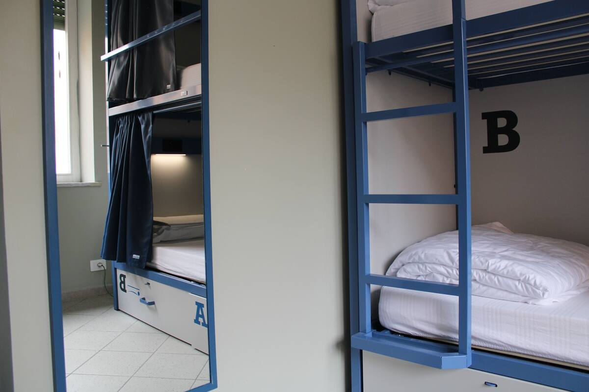 Habitación con literas, una ventana, la letra 'B' en la pared y una puerta con manija.