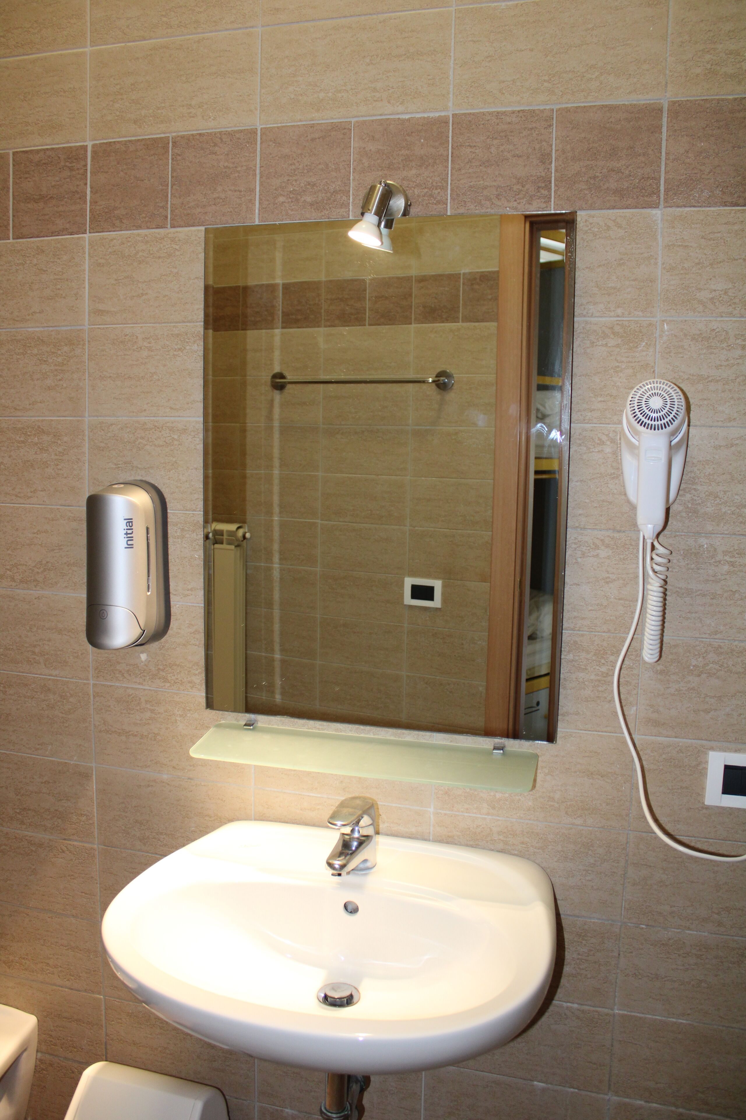 Un baño con lavamanos, espejo y secador de pelo fijado en la pared.