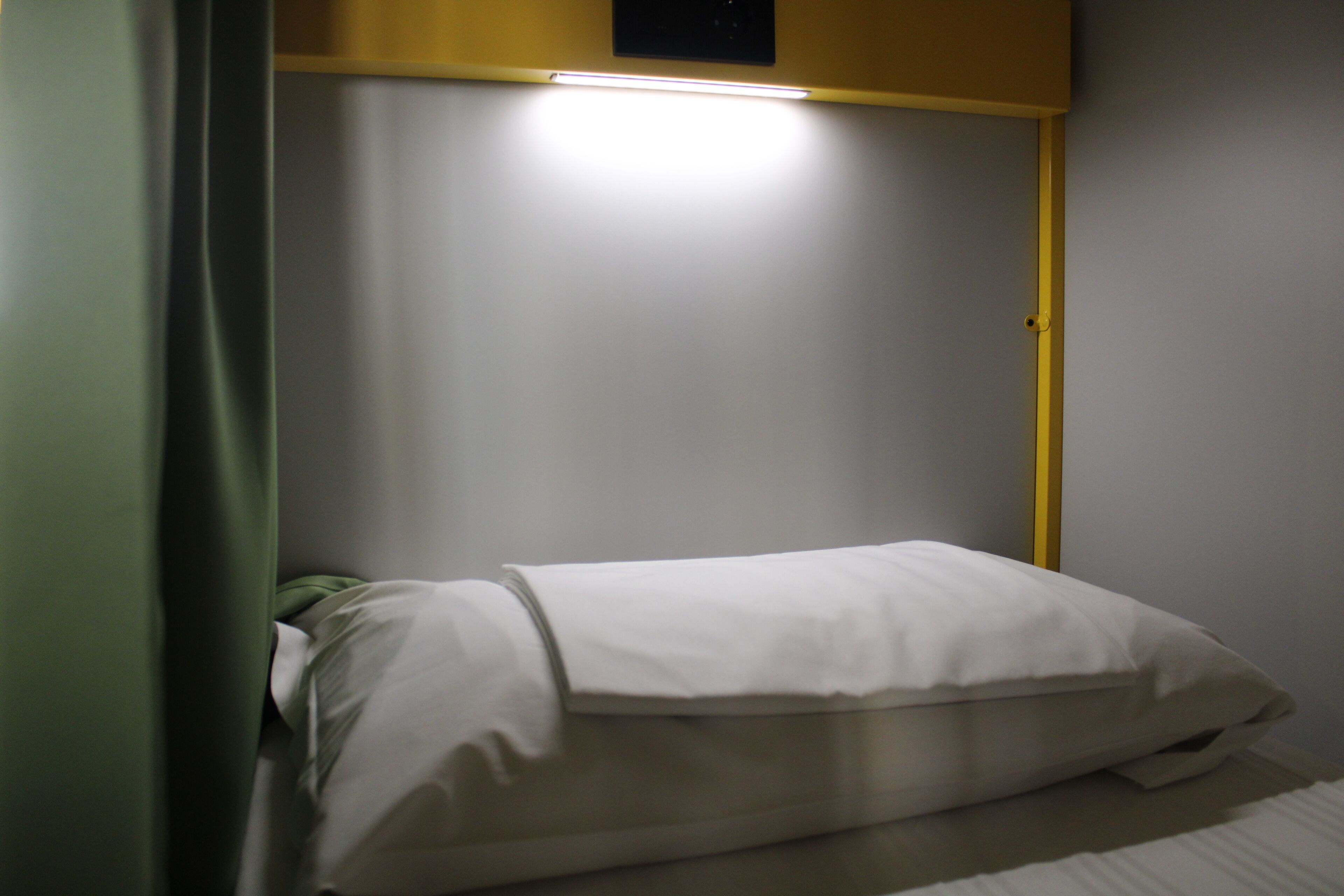 A small, single-bed room with a green curtain, a white pillow, and a yellow headboard.