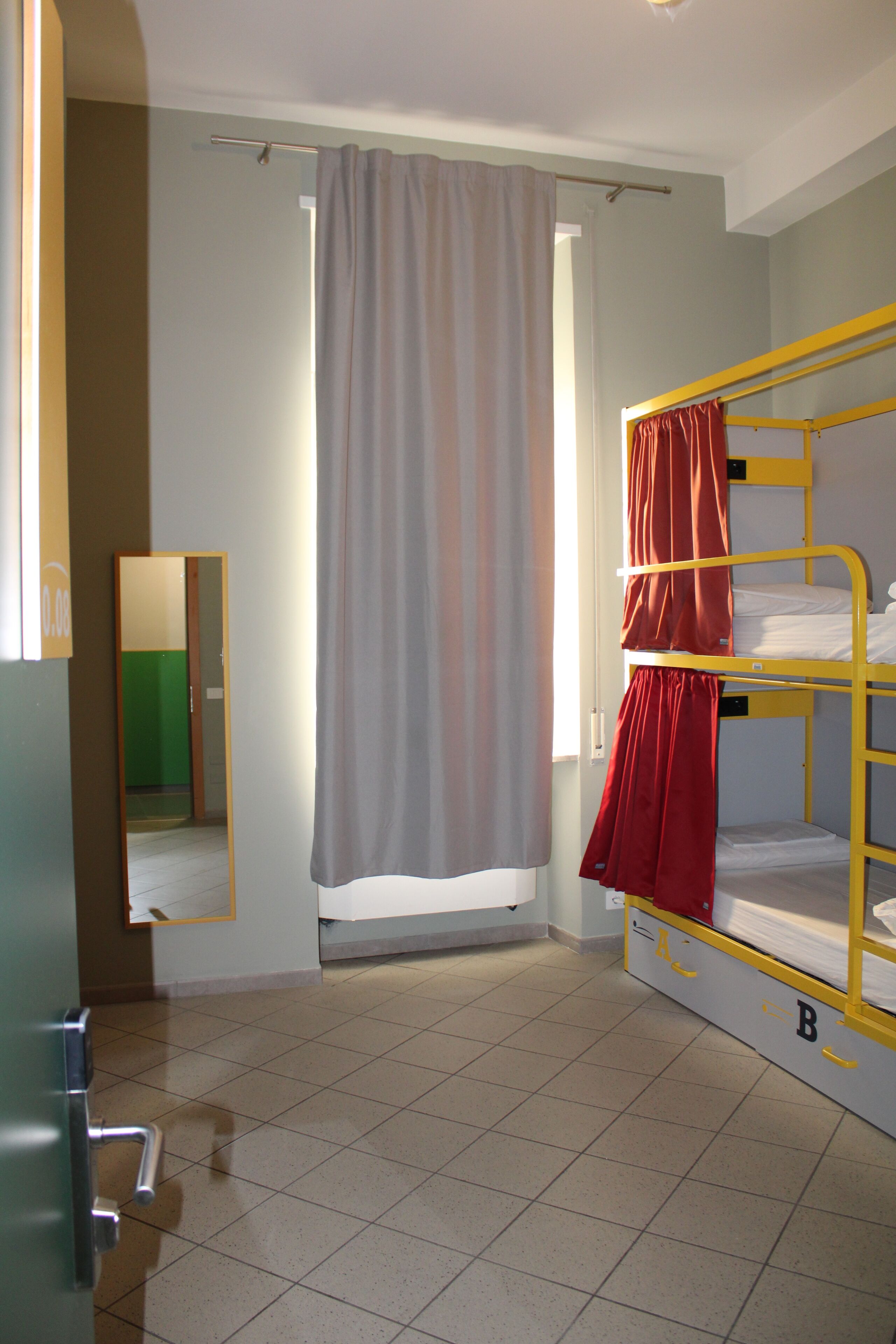 A dormitory room with bunk beds, a shower curtain, a mirror, and a tiled floor.