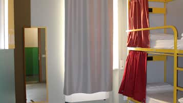 A dormitory room with bunk beds, a shower curtain, a mirror, and a tiled floor.