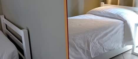 A hotel room with two beds, a nightstand, a wall-mounted lamp, and a tiled floor.