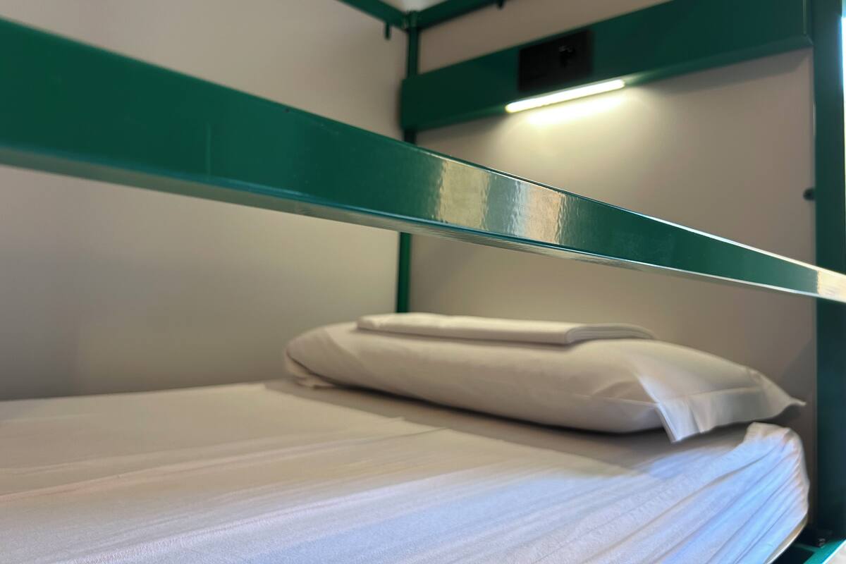 Una cama litera con estructura verde y ropa de cama blanca.