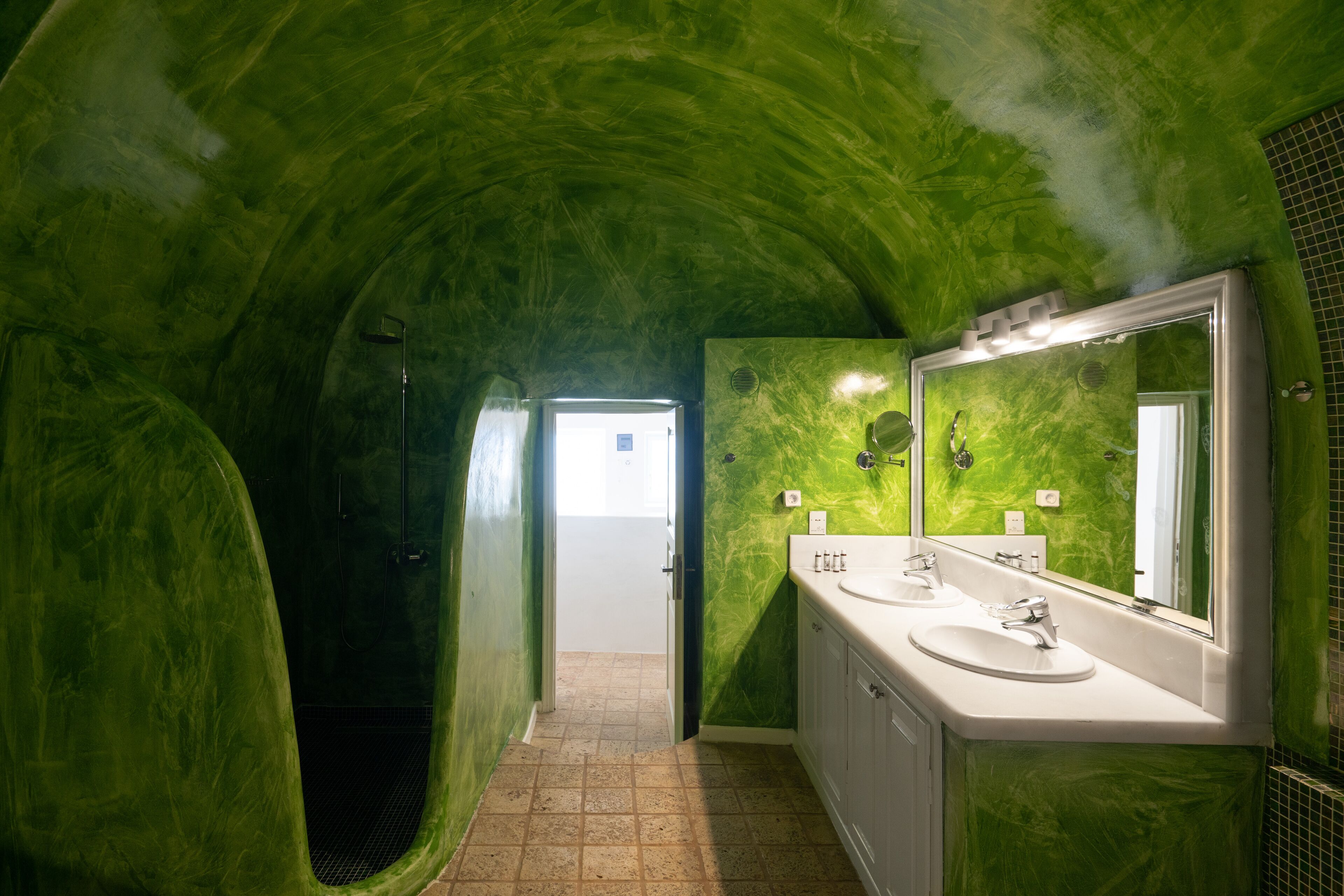 A bathroom with green walls, a shower, and a sink with a mirror.