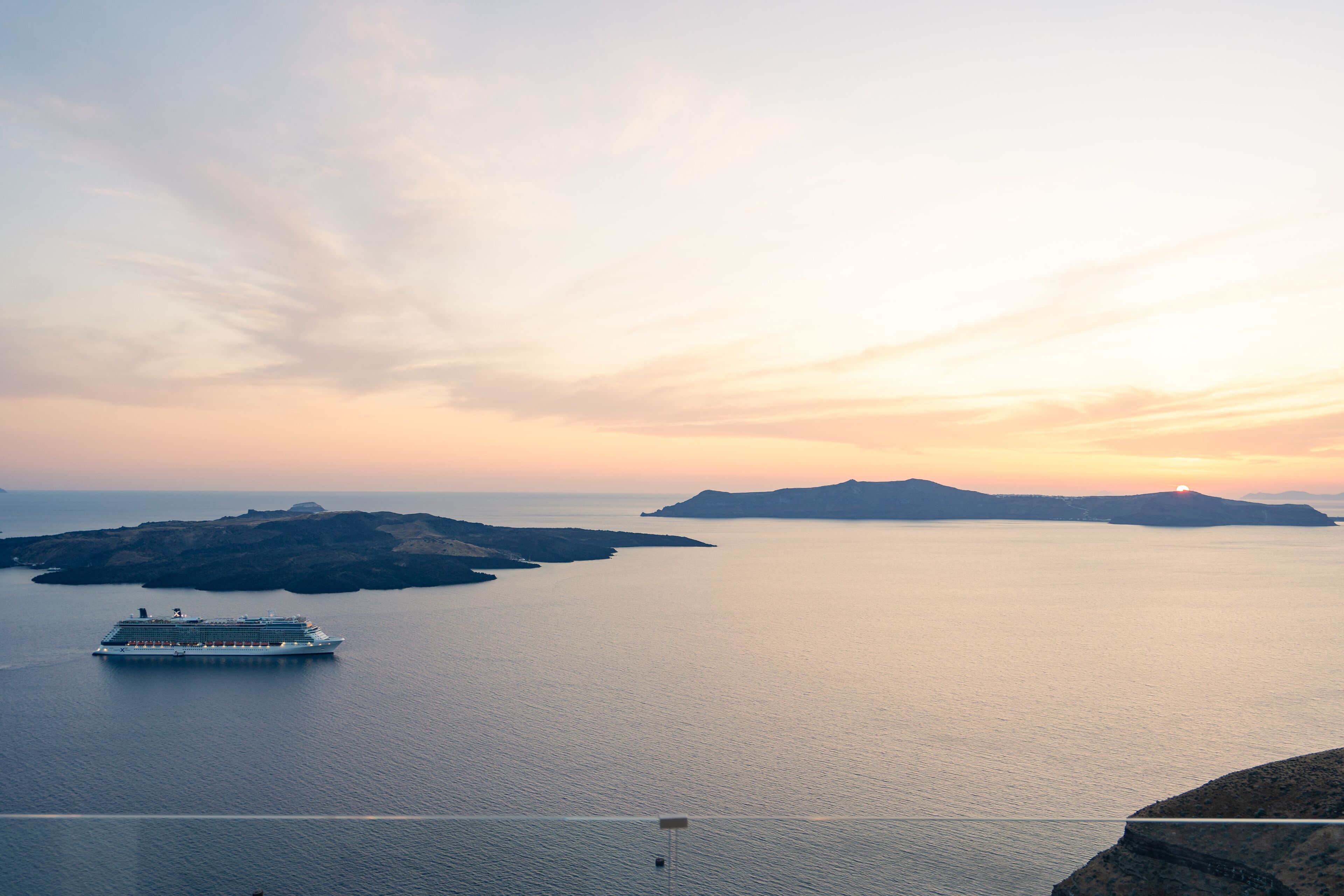 A cruise ship on calm waters with distant landforms and a clear sky.