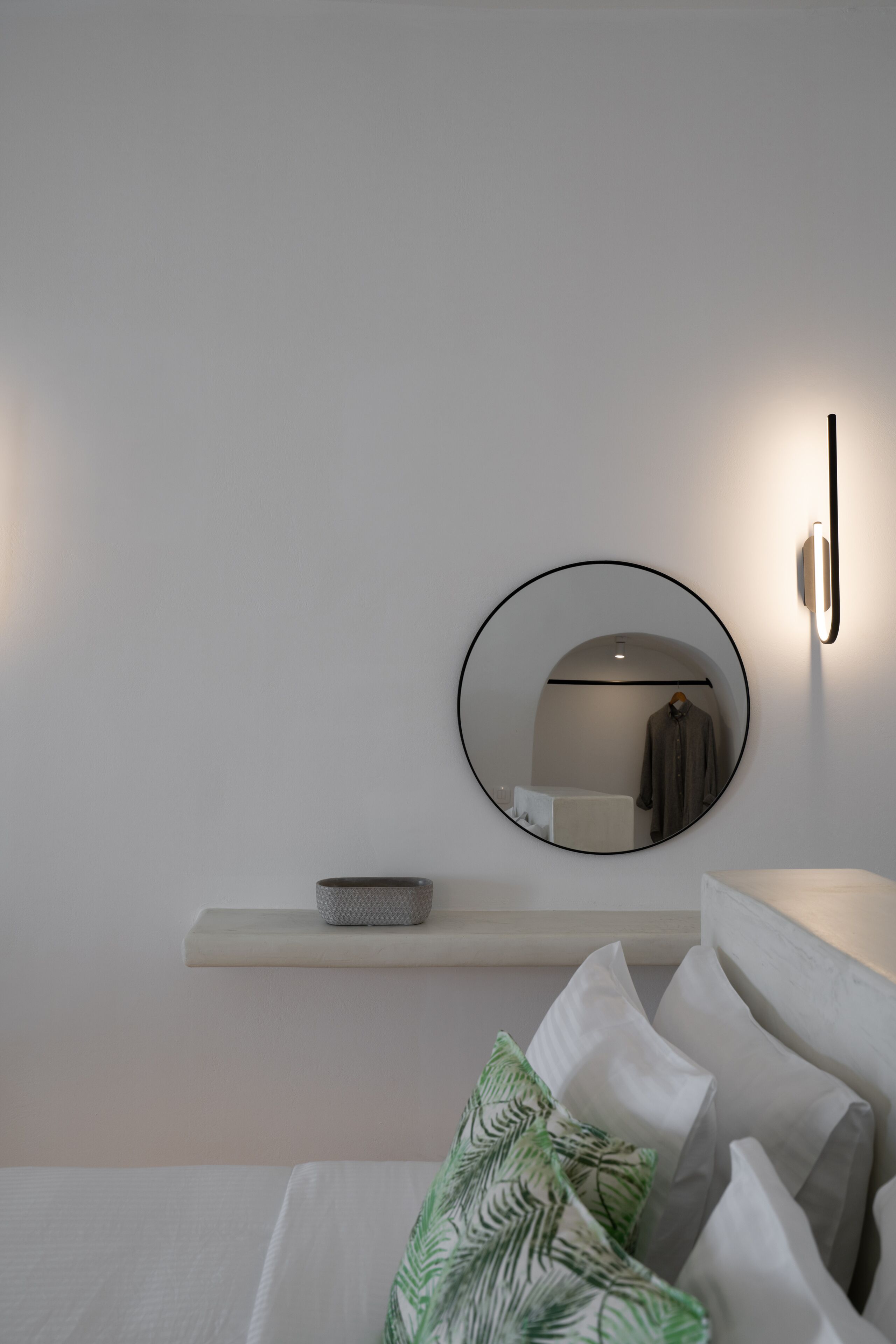 A modern bedroom with a round mirror, a bedside table, and a bed with pillows.