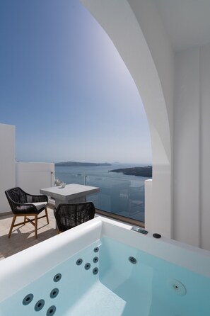A modern balcony with a hot tub, two wicker chairs, and a table.