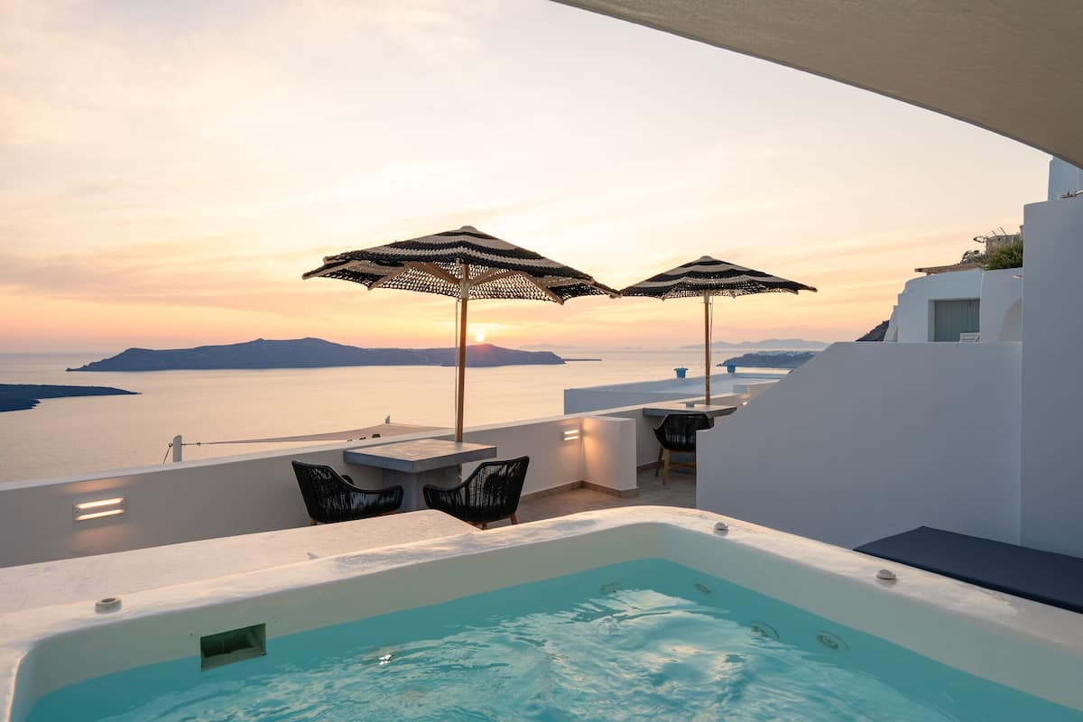 Ein Poolbereich auf dem Dach mit zwei Sonnenschirmen, einem Whirlpool und Blick auf das Meer bei Sonnenuntergang.