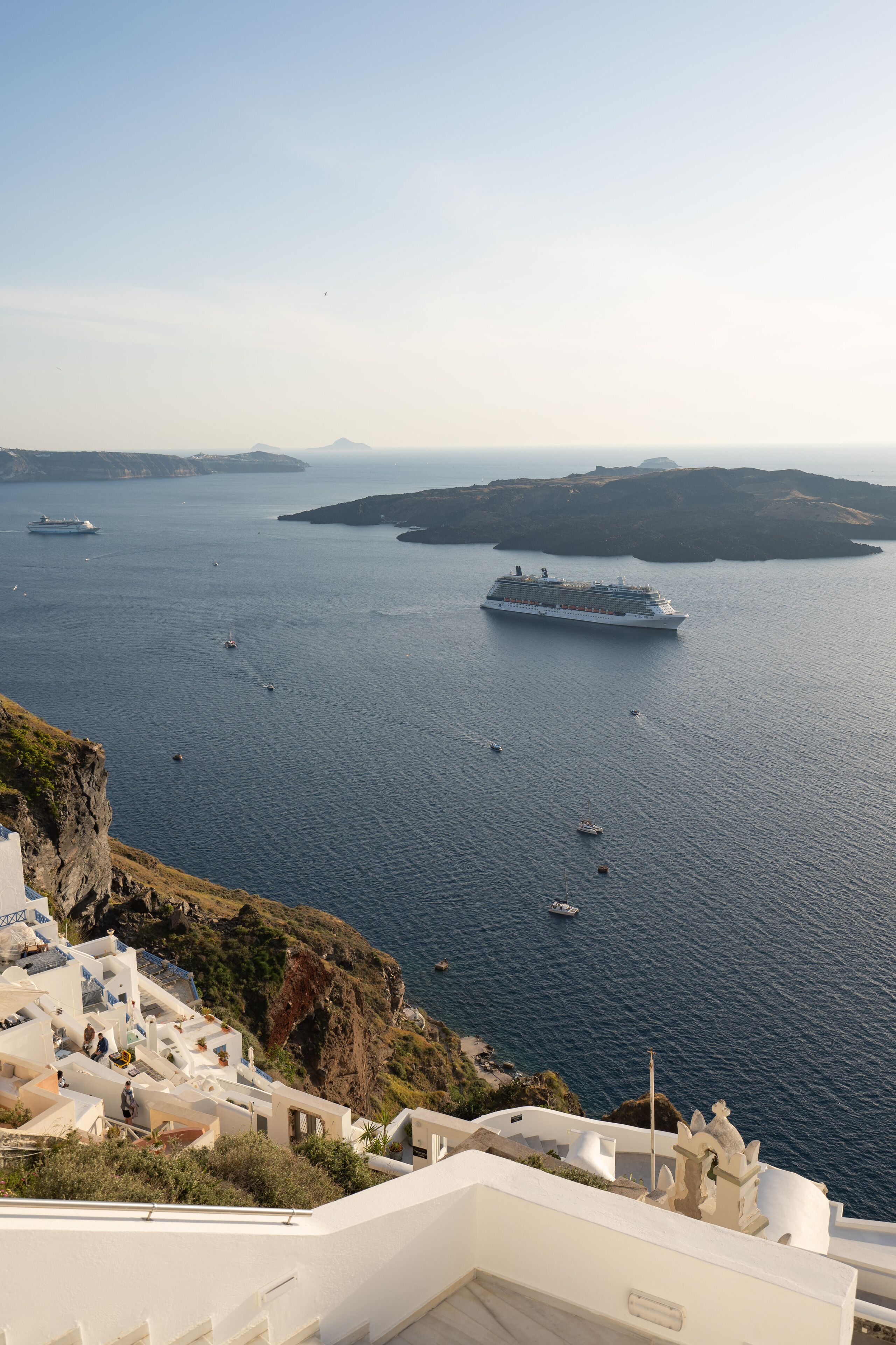 Eine Küstenansicht mit einem Kreuzfahrtschiff, Booten und weißen Gebäuden mit Stufen, die zum Meer hinabführen.