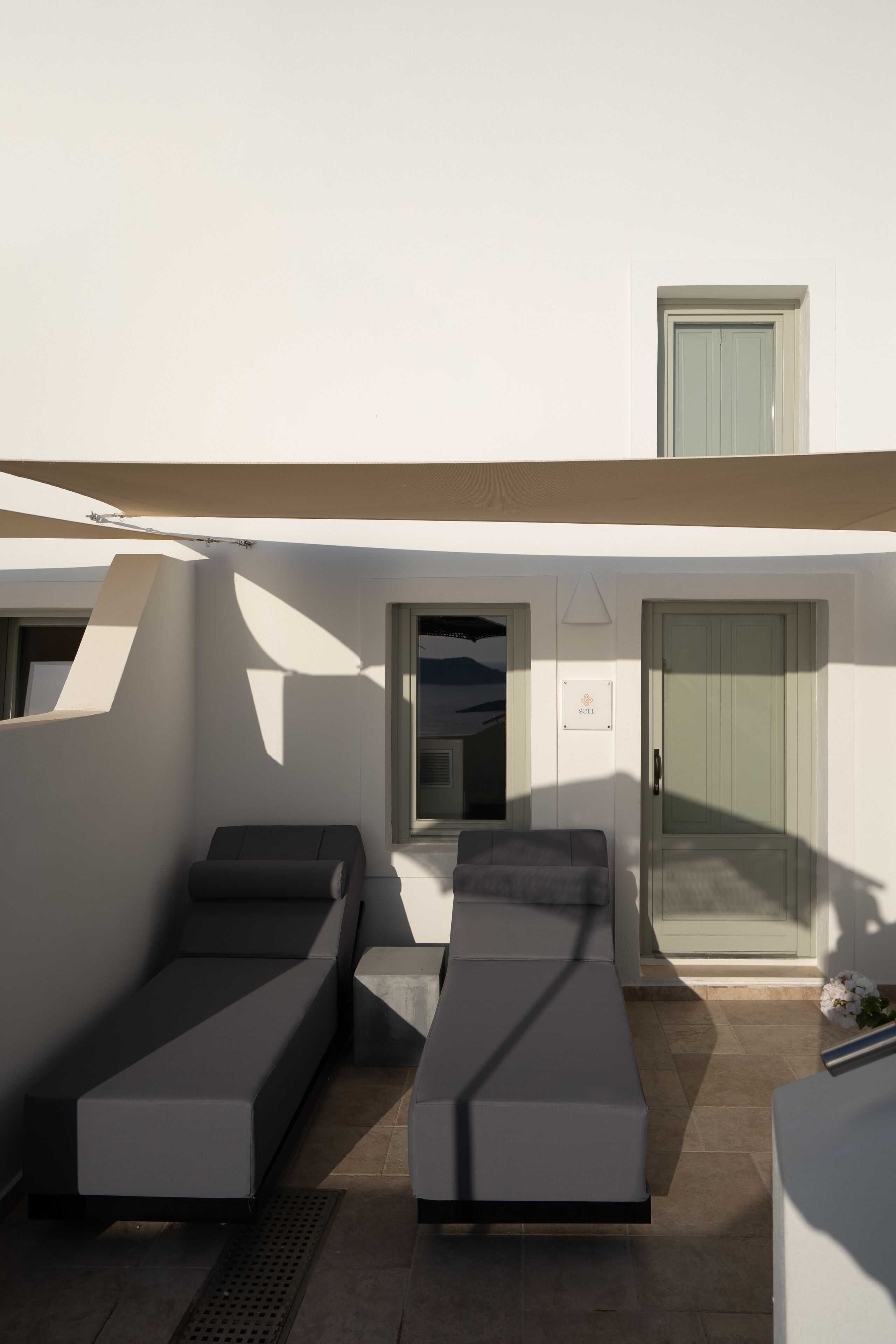 A modern outdoor lounge area with two reclining chairs, a small table, and a door.