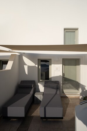 A modern outdoor lounge area with two reclining chairs, a small table, and a door.