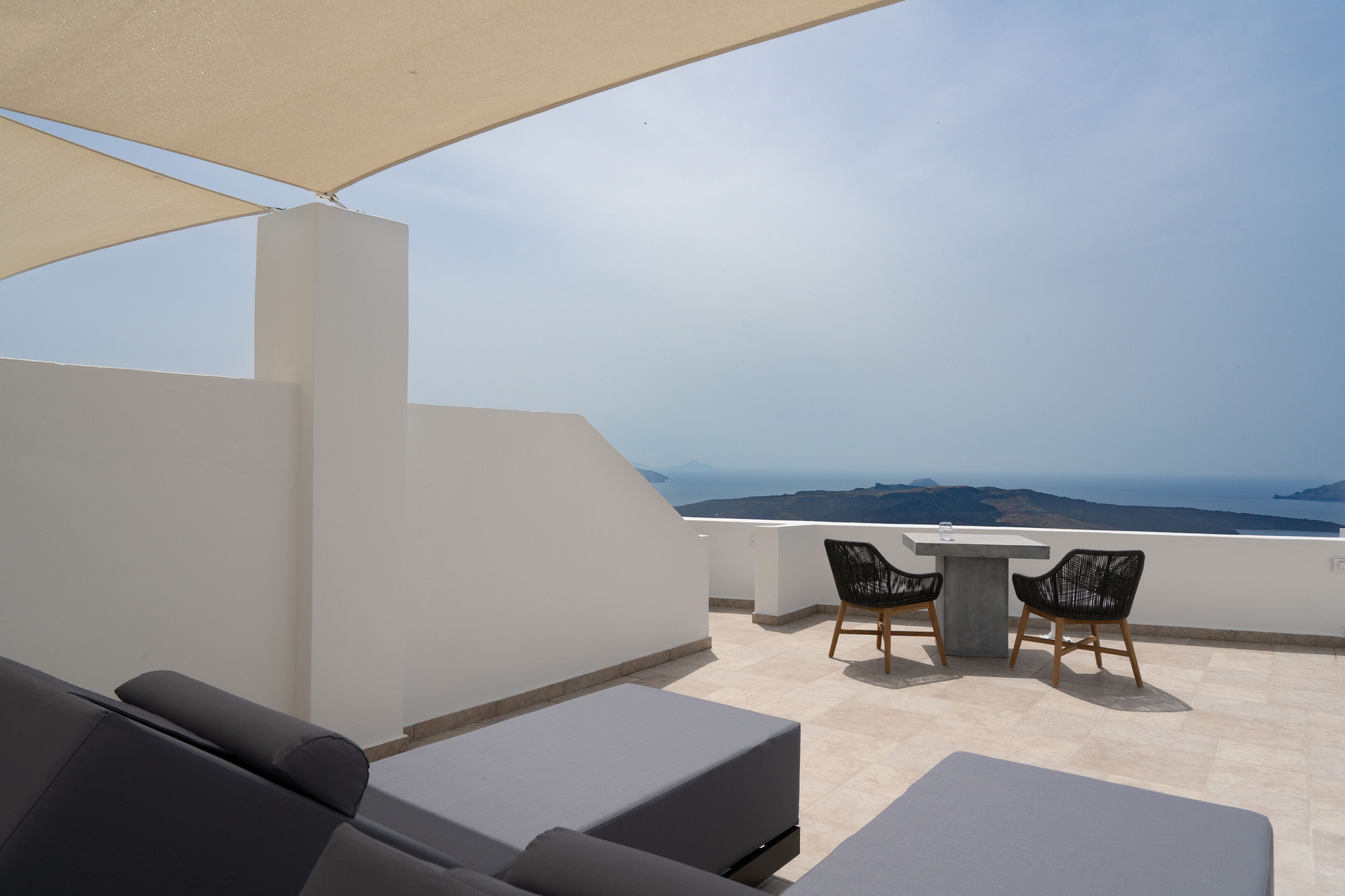 Une terrasse sur le toit, aménagée avec un canapé, deux fauteuils et une table, offrant une vue panoramique sur la mer et le paysage lointain.