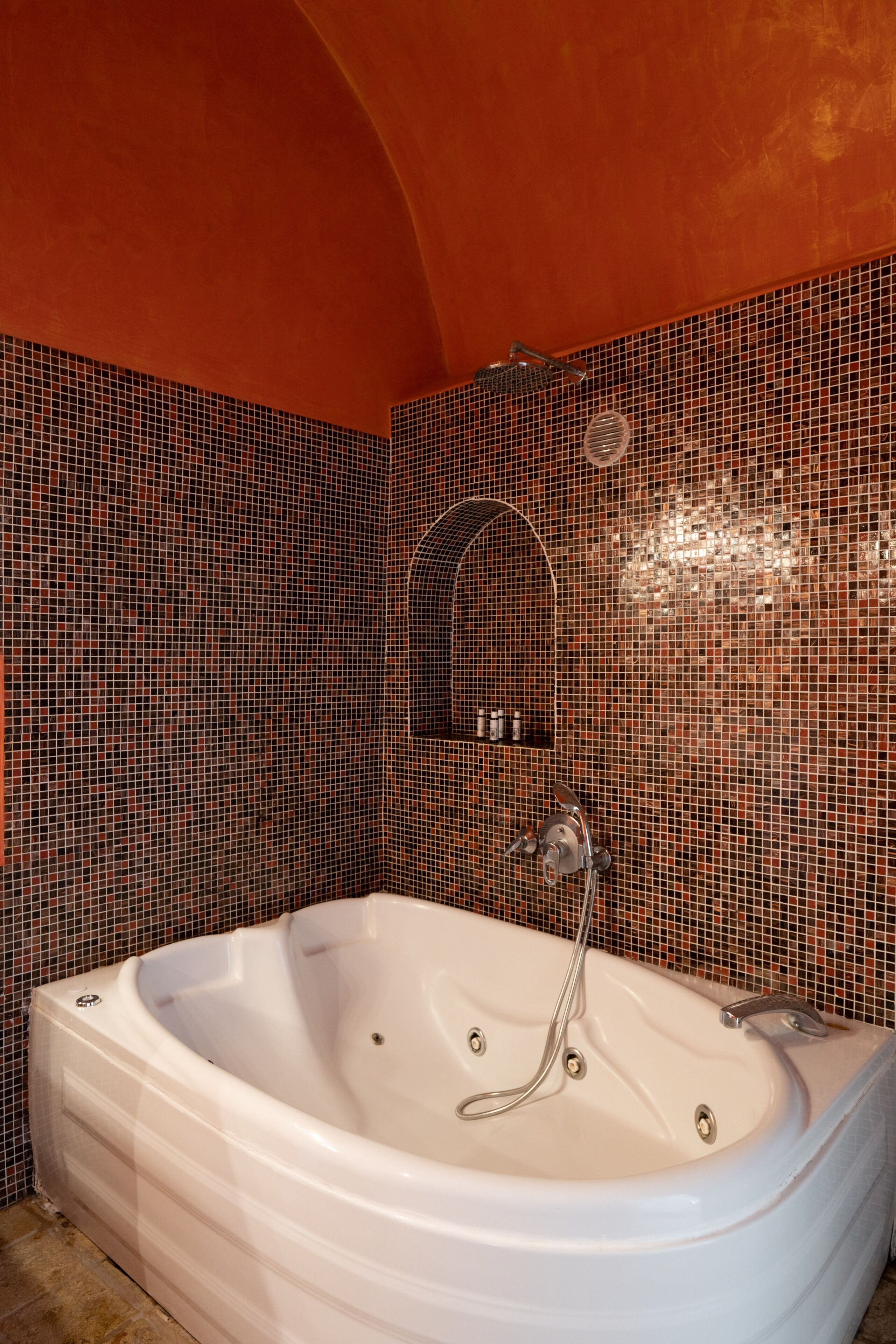 A modern bathroom with a large white bathtub, a shower with a curved wall, and a tiled mosaic wall.