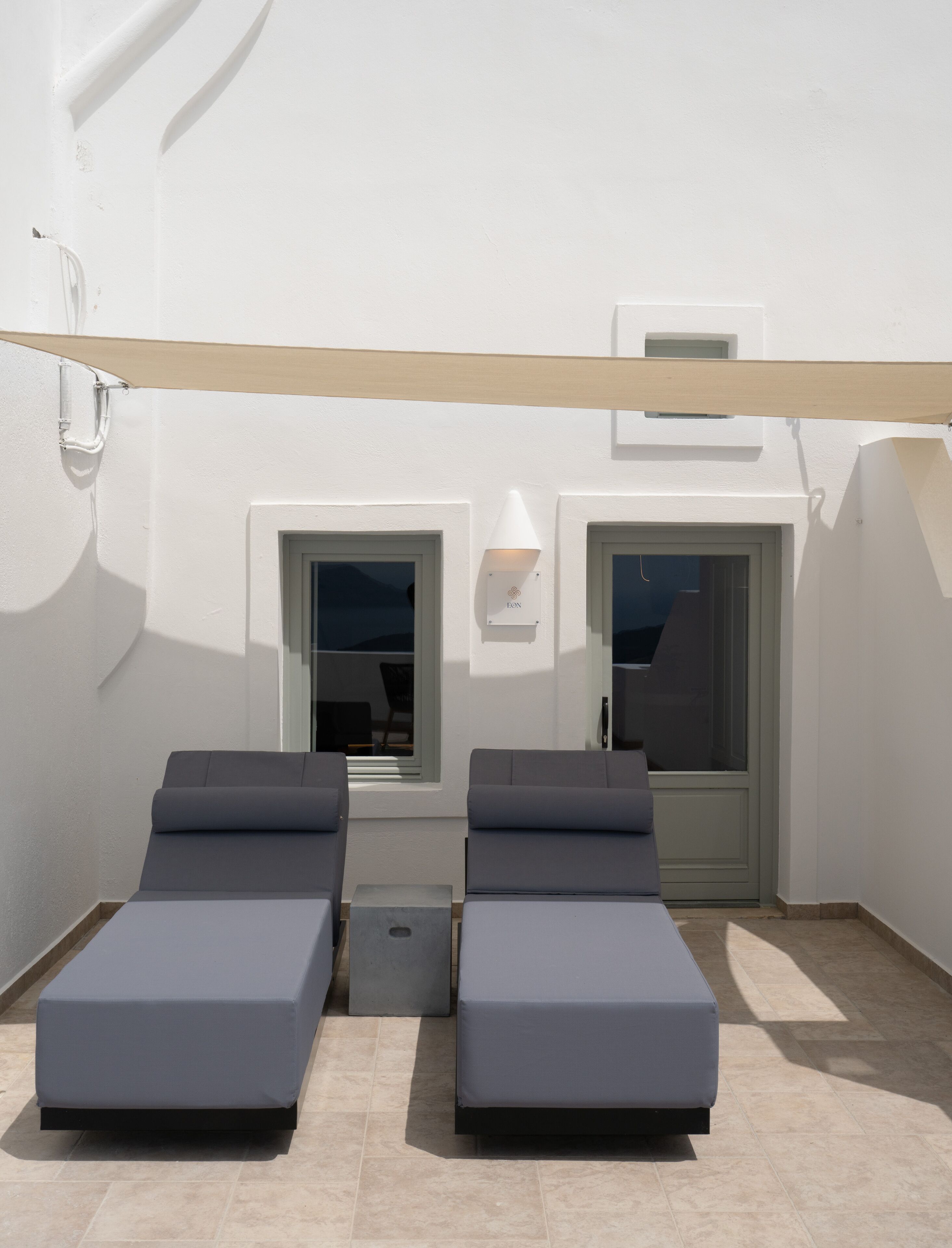 A rooftop terrace with two lounge chairs and a small table, a white awning, and a door with a window.
