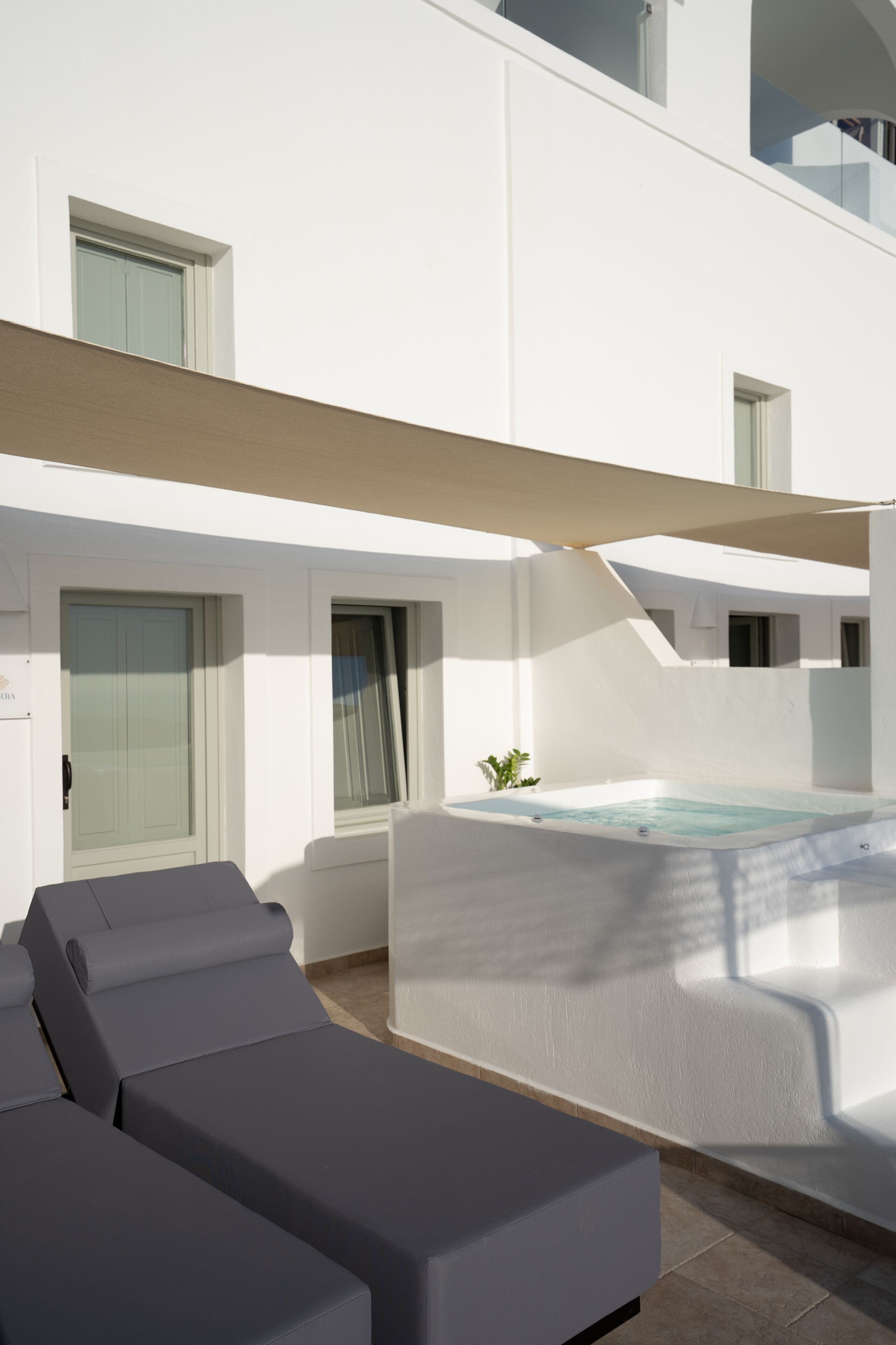 Un área de piscina moderna al aire libre, con un jacuzzi, sillas de descanso y una zona de estar cubierta.