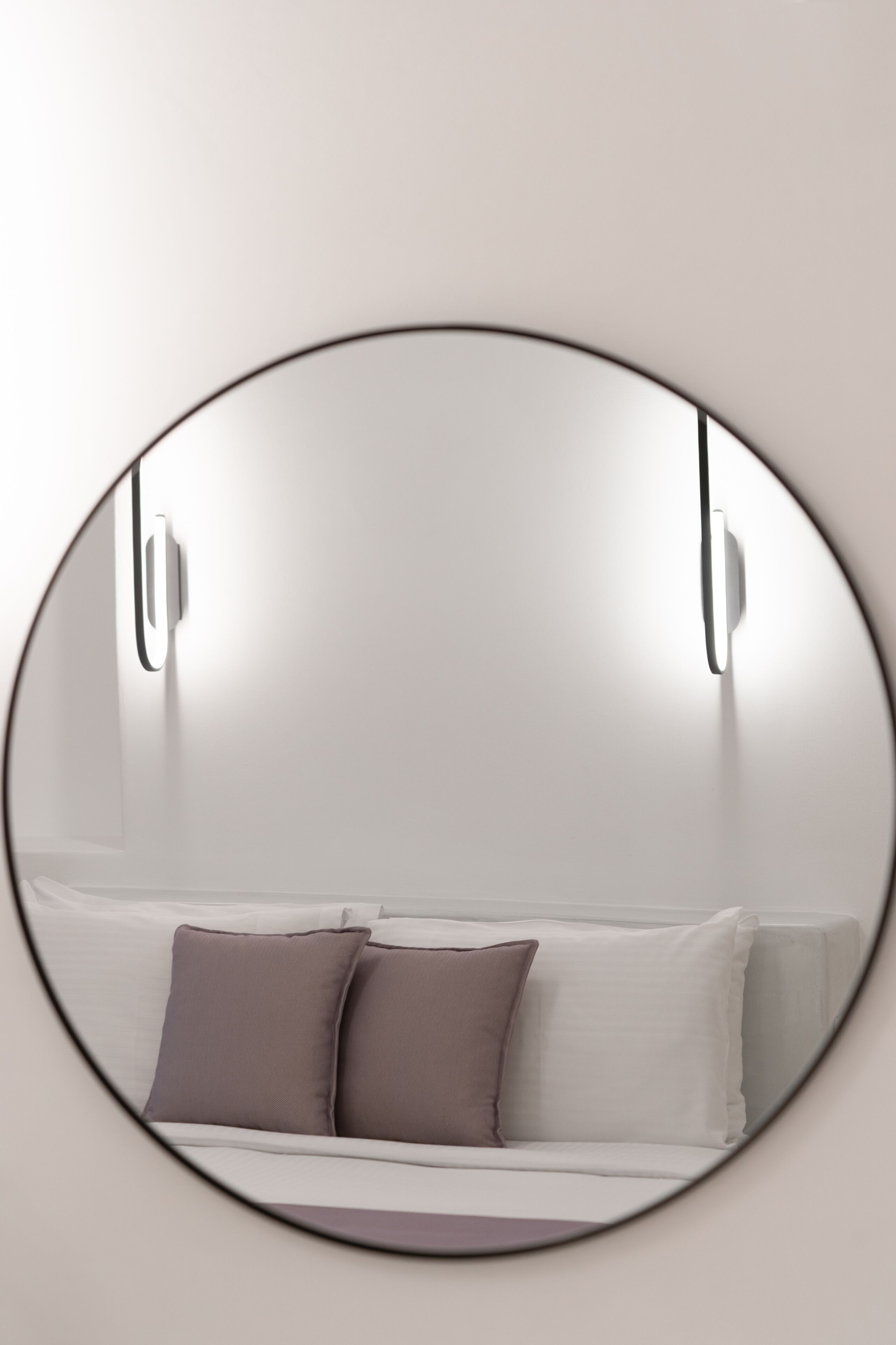 A circular mirror reflecting a bed with white and gray bedding and two pillows.
