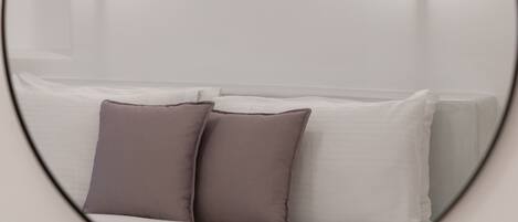 A circular mirror reflecting a bed with white and gray bedding and two pillows.