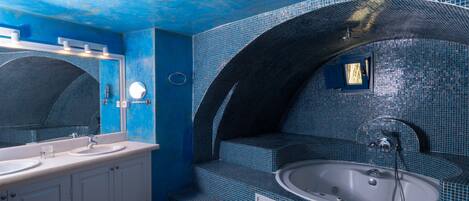 A bathroom with a blue tiled wall, a large mirror, a sink, and a bathtub.