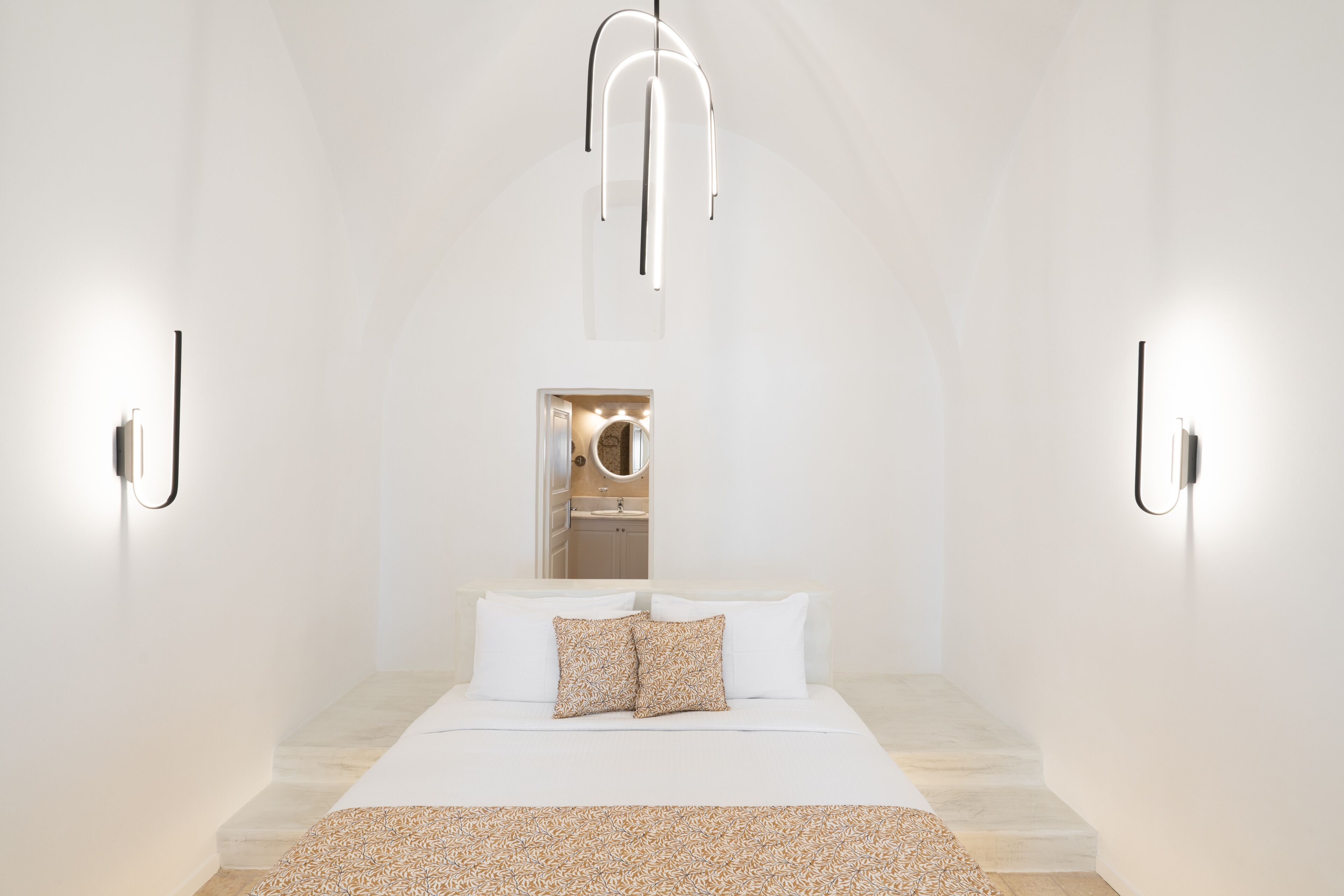 Un dormitorio moderno con una cama centrada en la habitación, un espejo sobre la cama y lámparas fijadas a la pared.
