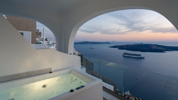 Habitación de hotel moderna con un amplio ventanal de arco que ofrece vistas al mar y un crucero.