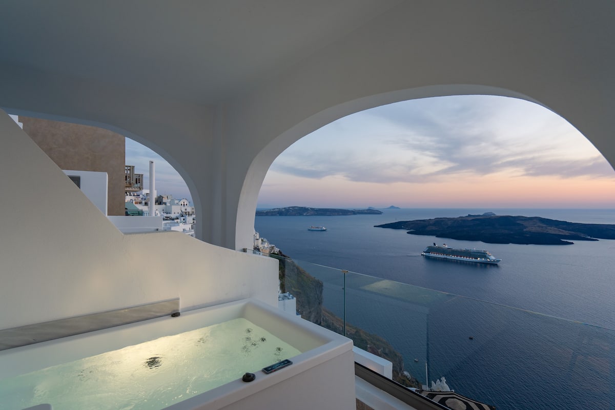 Ein modernes Hotelzimmer mit einem großen Bogenfenster, das Meer und ein Kreuzfahrtschiff zeigt.
