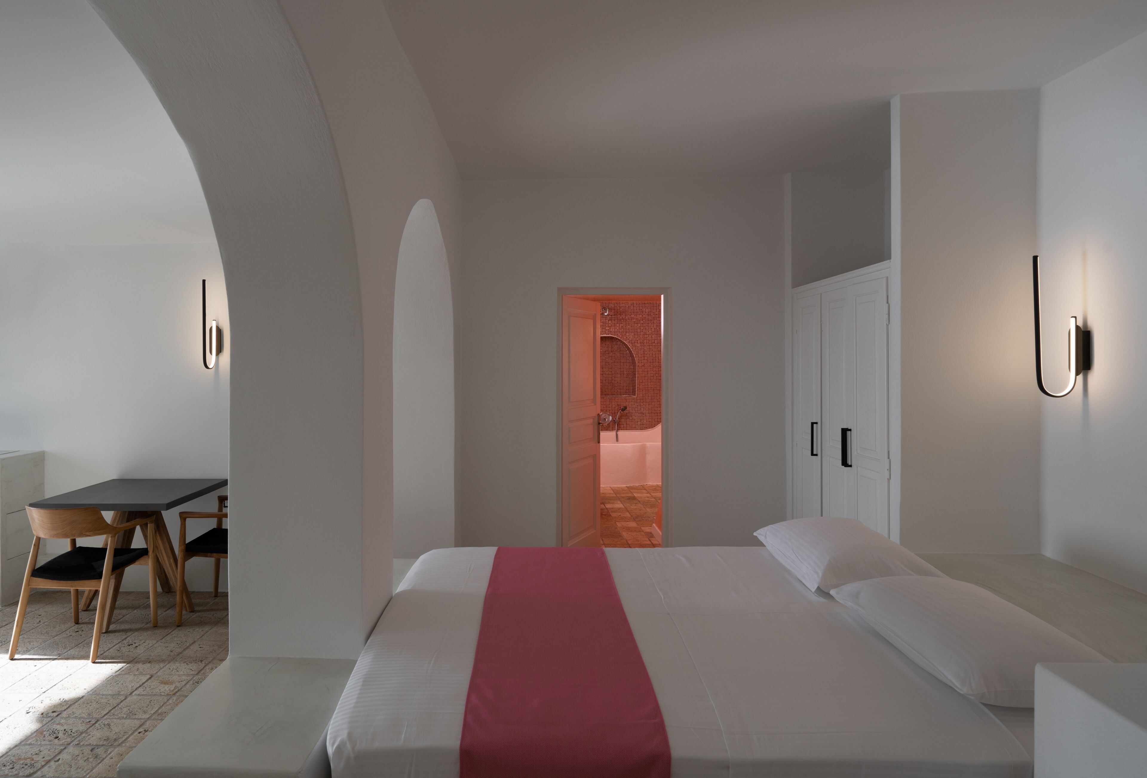 A modern hotel room with a large bed, a desk with chairs, and a bathroom visible through an open door.