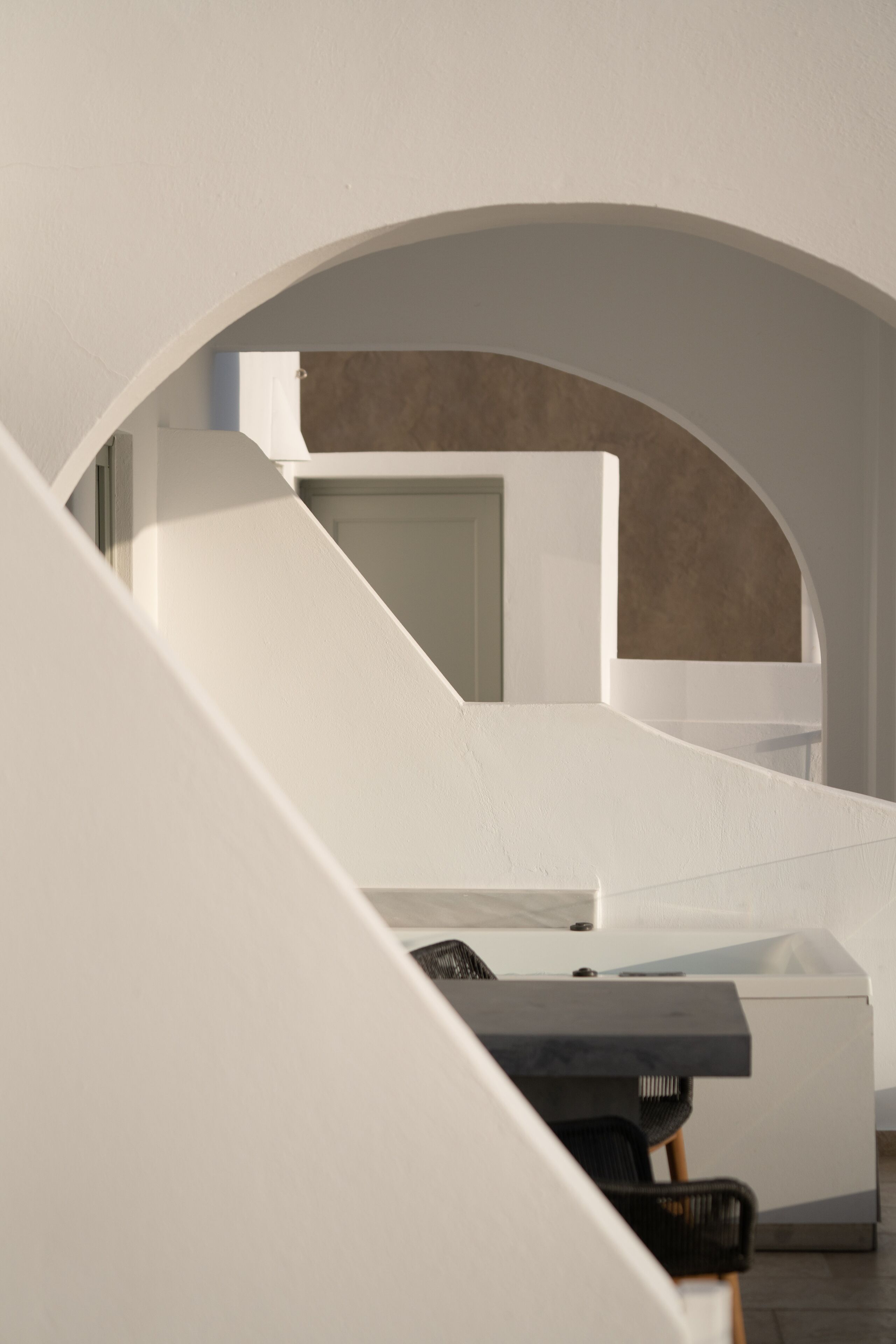 A modern interior with a minimalist staircase, a white reception desk, and a view through an archway.