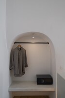 A room with a white wall, a wooden hanger holding a grey shirt, and a black electronic device on a shelf.