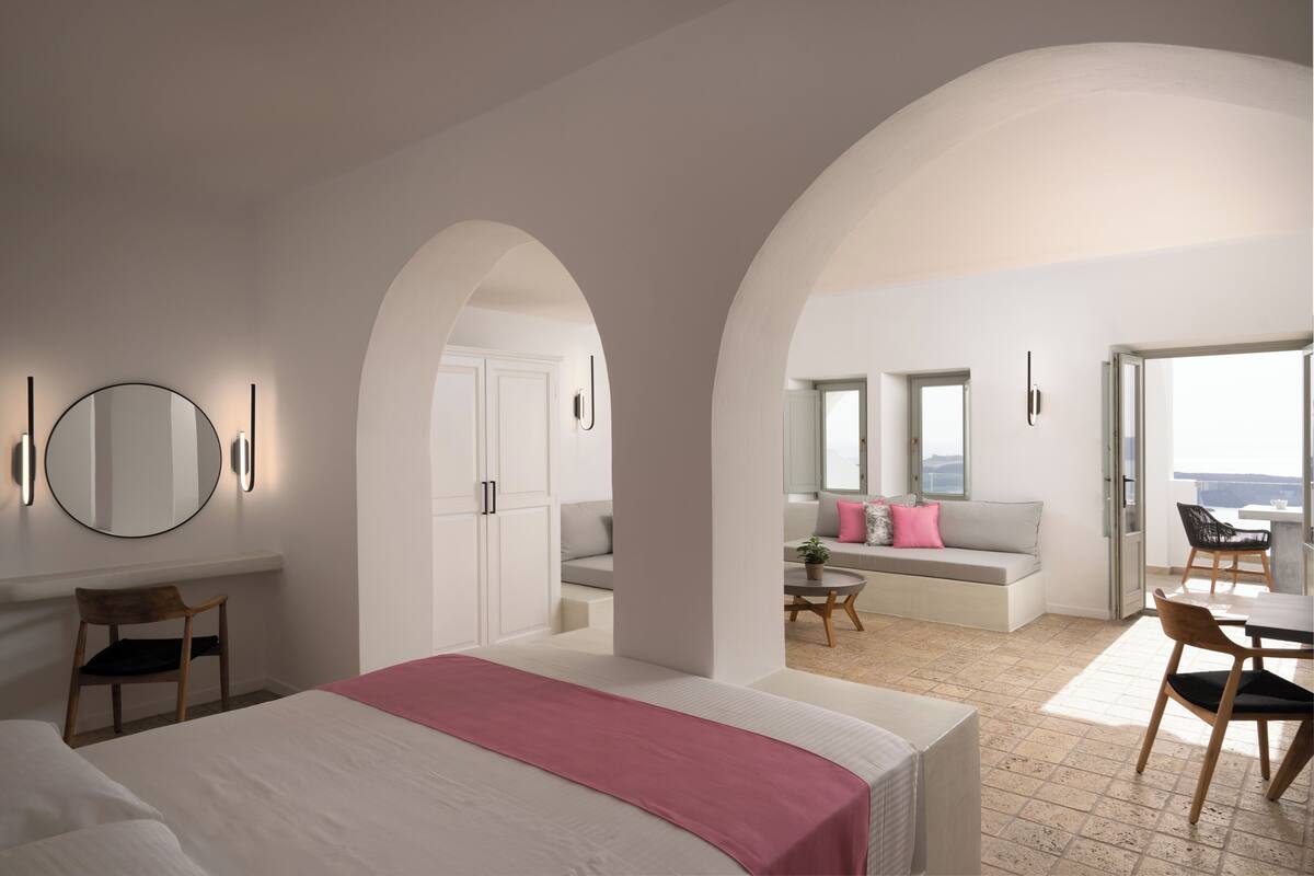 Ein modernes Hotelzimmer mit einem großen Bett, einer Sitzecke mit Sofa und Sesseln sowie einem Balkon mit Aussicht.
