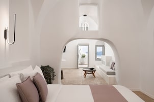Un dormitorio moderno con una cama grande, una mesita redonda y vistas a un balcón con asientos a través de un arco.
