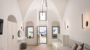 Un interior moderno con techos altos, puertas arqueadas, una zona de estar con sofá y cojines, una mesita con un cuenco y vistas a través de las ventanas.