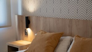 A neatly made bed with two pillows, a wooden headboard, and a bedside table with a lamp. - Urbana Class Hotel (Mendoza)