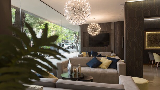 A modern living room with a sofa set, two side tables, decorative vases, and a large spherical light fixture. - Urbana Class Hotel (Mendoza)