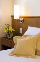 Una cama con almohadas de diseño amarillo, una mesita de noche con un florero de flores amarillas y una lámpara de pared.