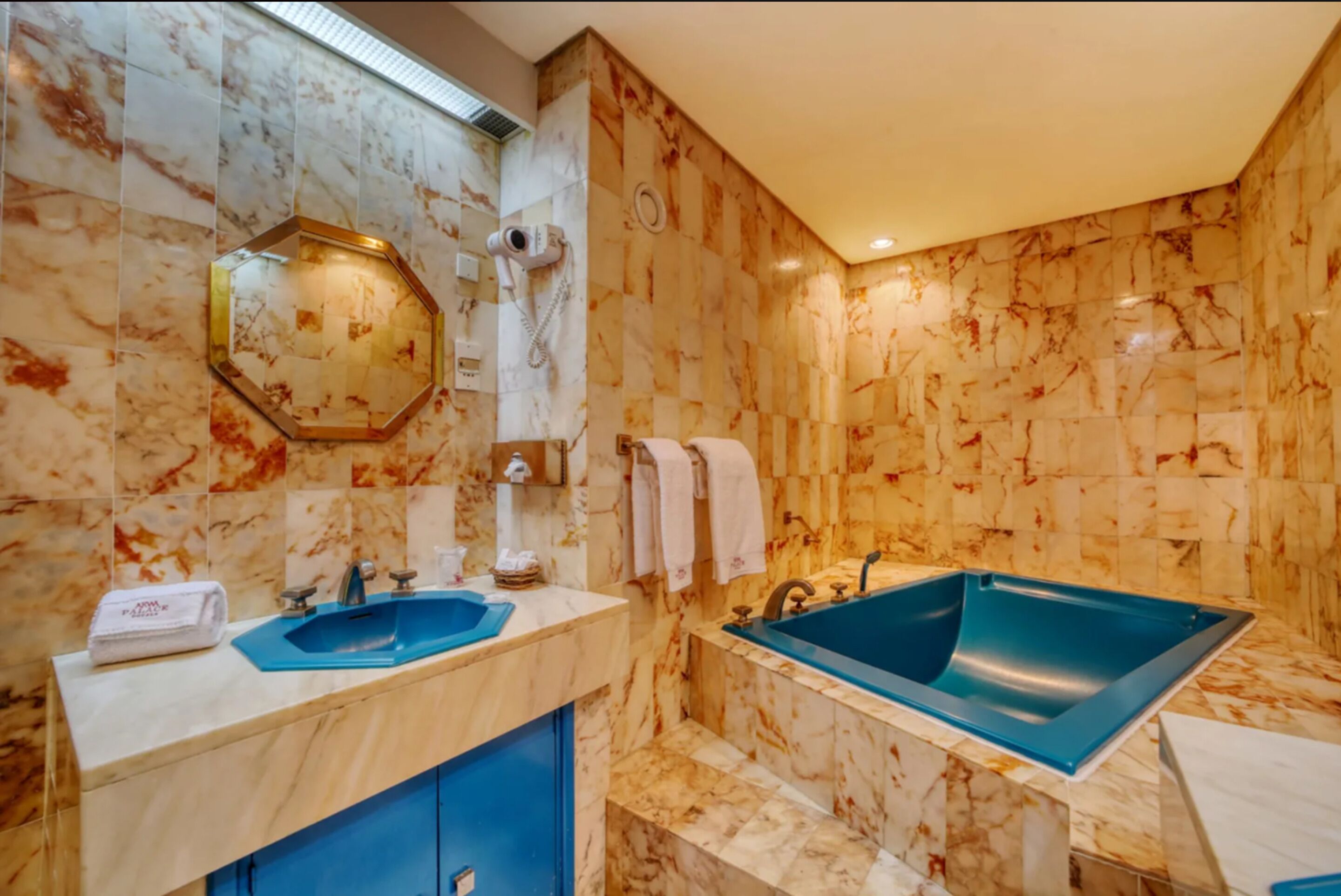 Un baño con paredes de mármol, un espejo grande, un lavabo, una bañera y un perchero para toallas.