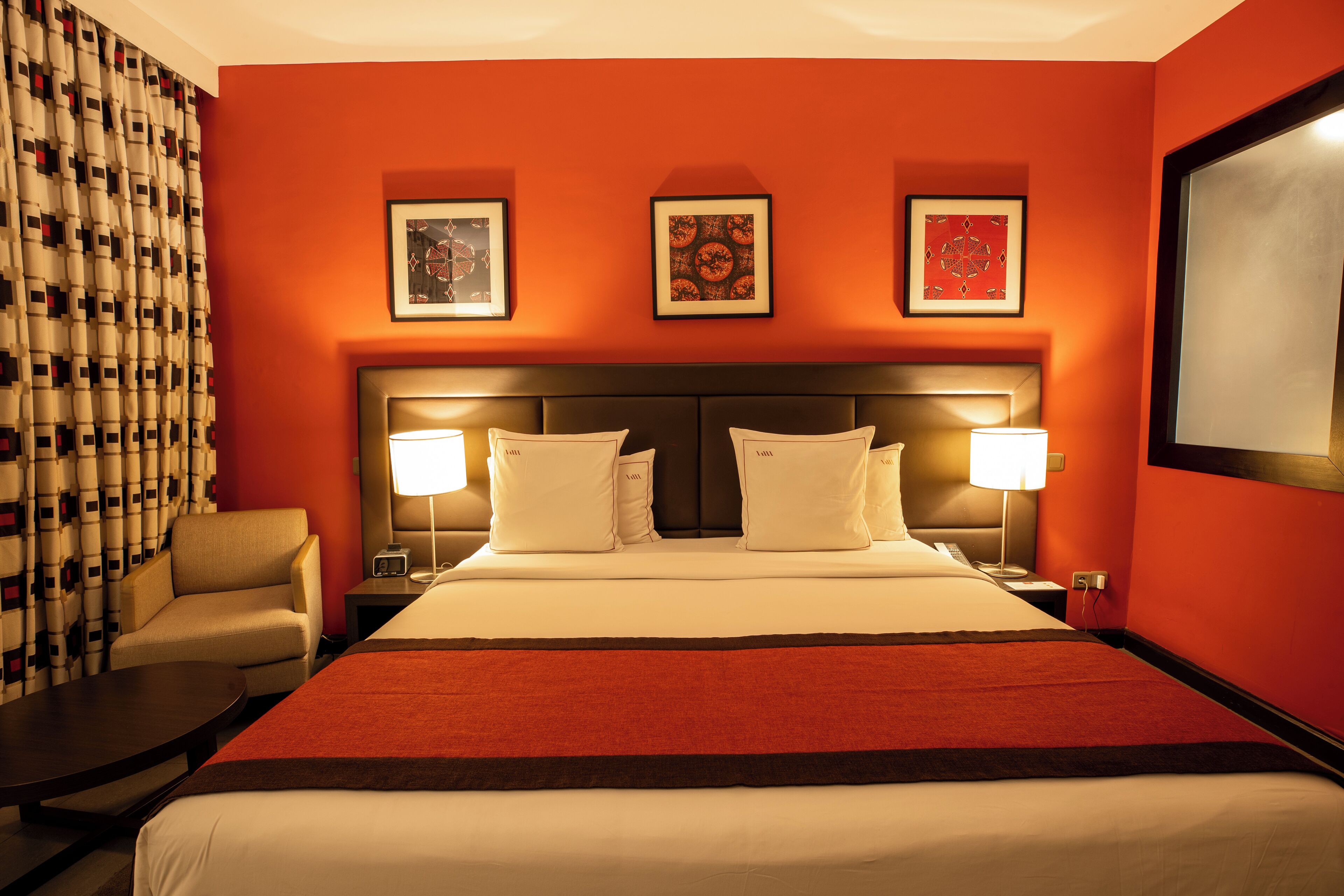 A hotel room with a large bed, two bedside tables with lamps, a chair, and three framed pictures on the wall.