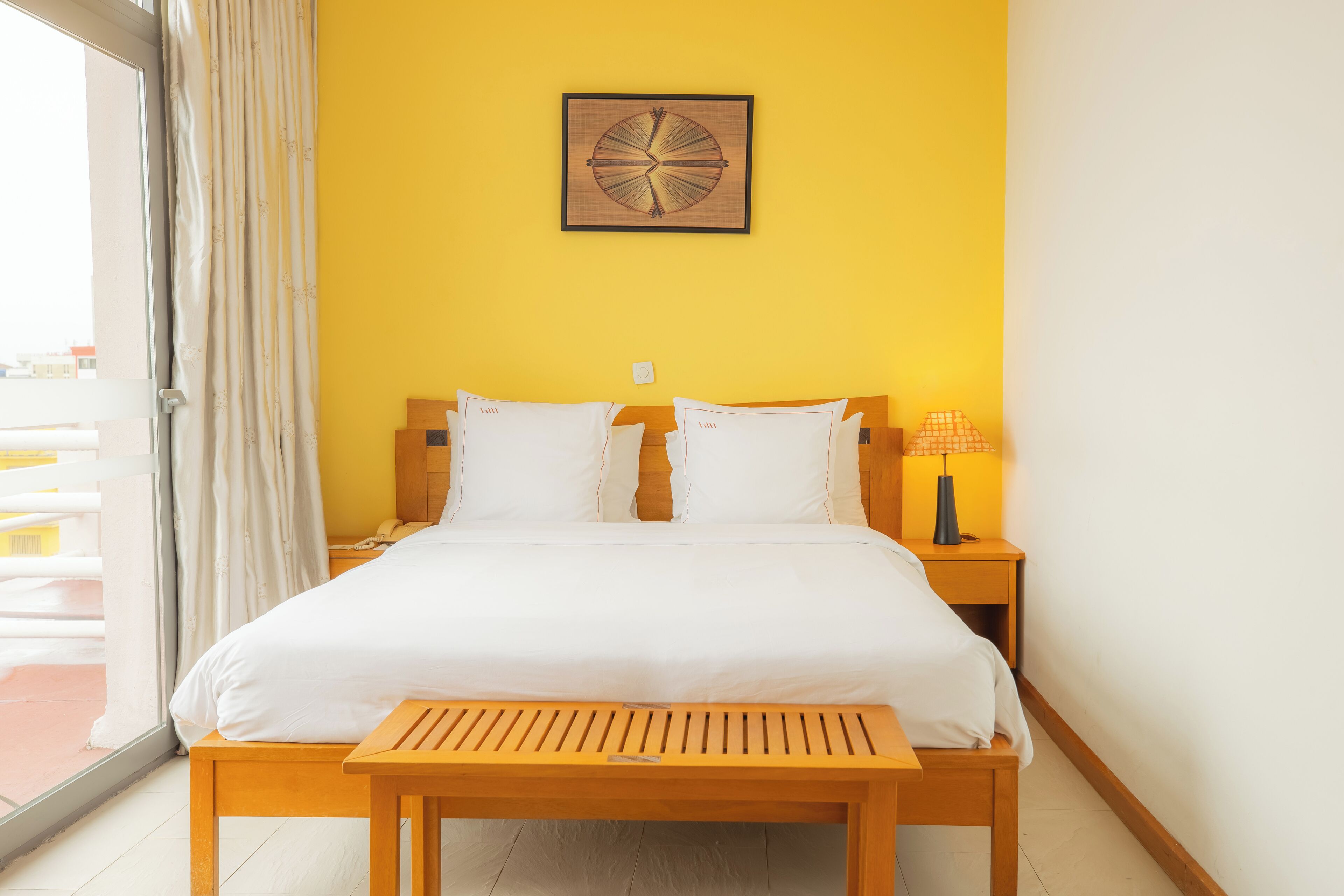 A hotel room with a bed, a wooden nightstand, a lamp, and a wall clock.