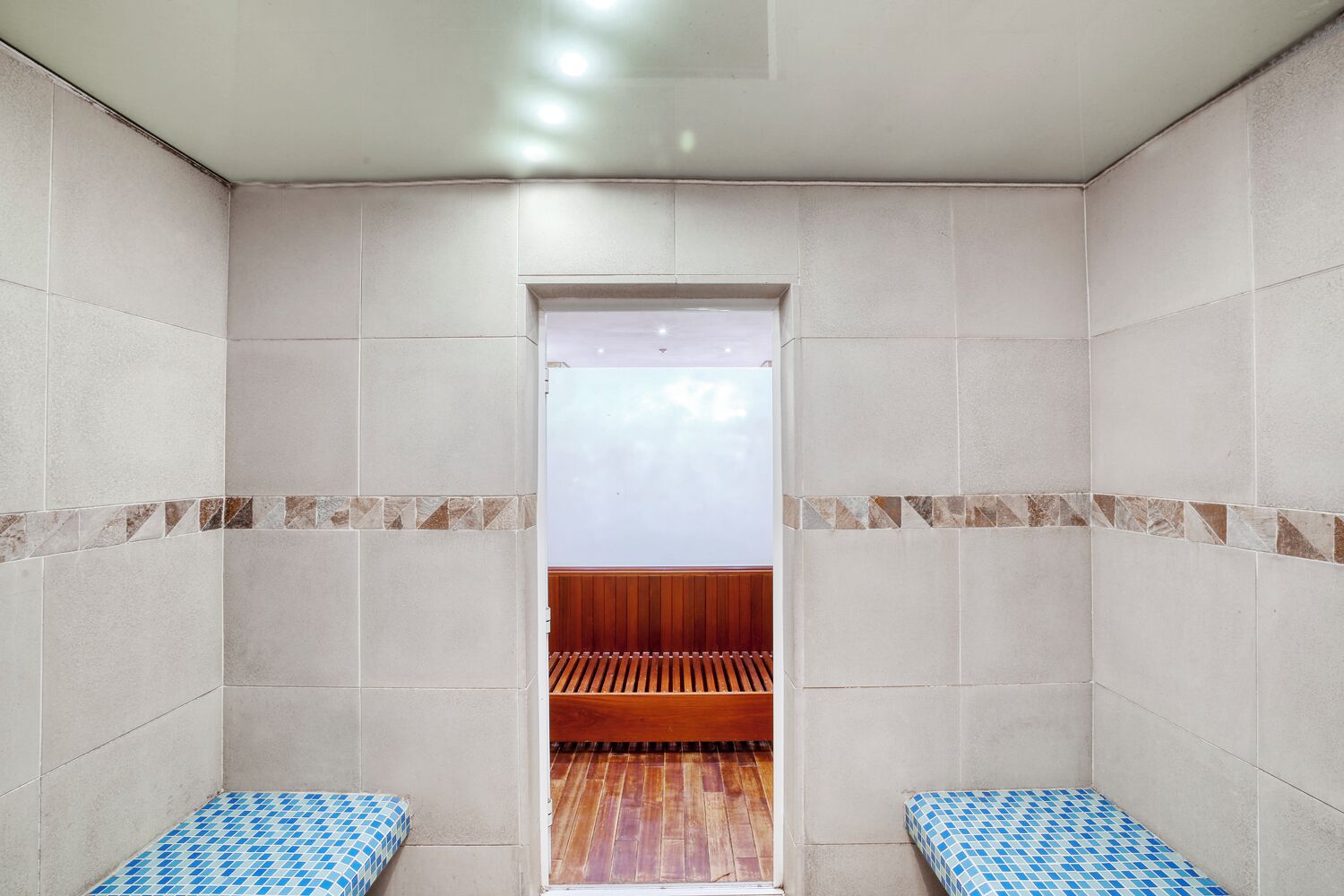 Una sala de sauna con paredes y suelo de baldosas y un banco de madera.