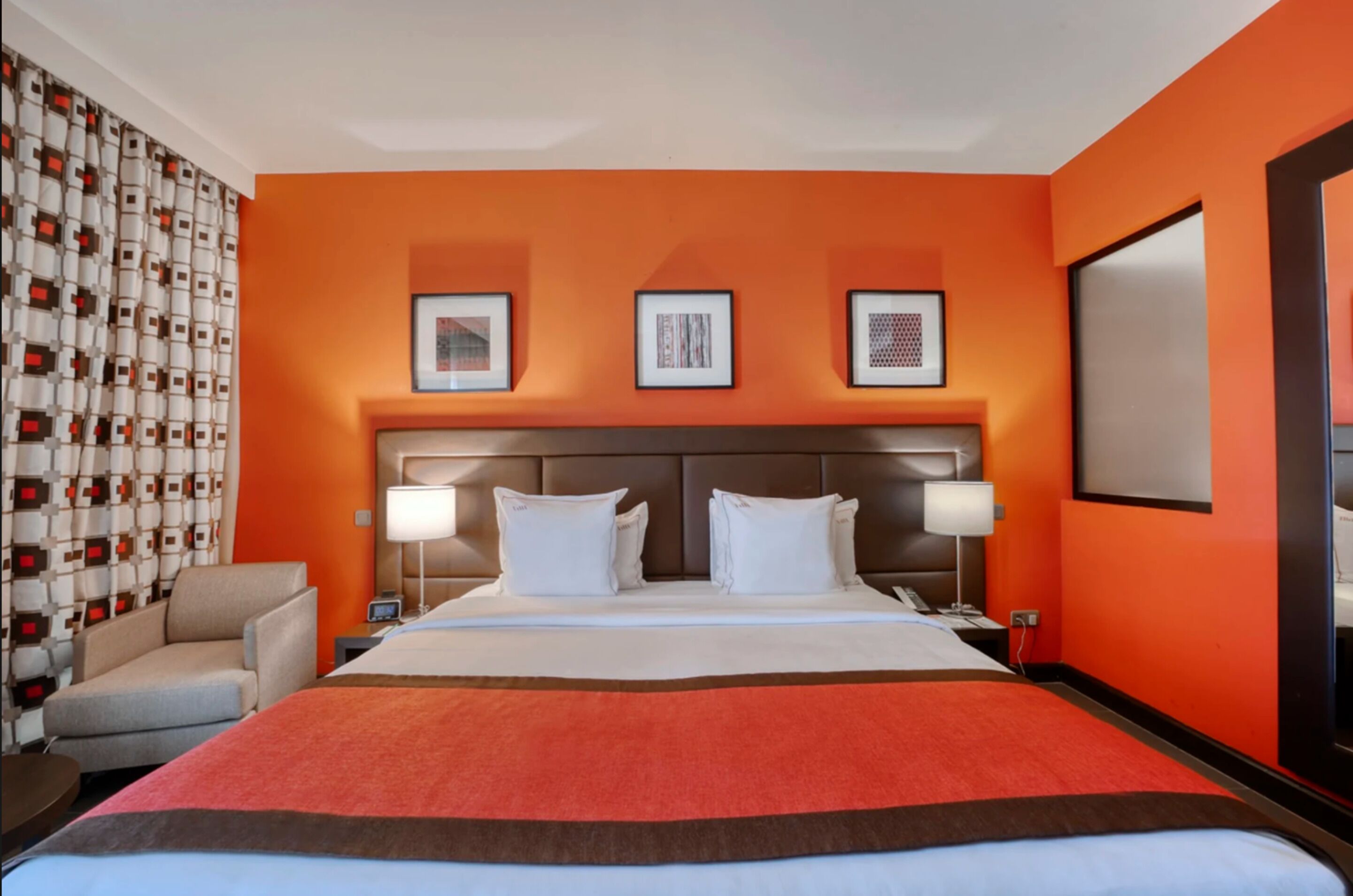 Habitación de hotel con una cama grande, dos mesitas de noche, una silla y una pared con tres cuadros enmarcados.