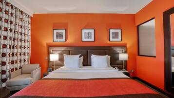 Habitación de hotel con una cama grande, dos mesitas de noche, una silla y una pared con tres cuadros enmarcados.
