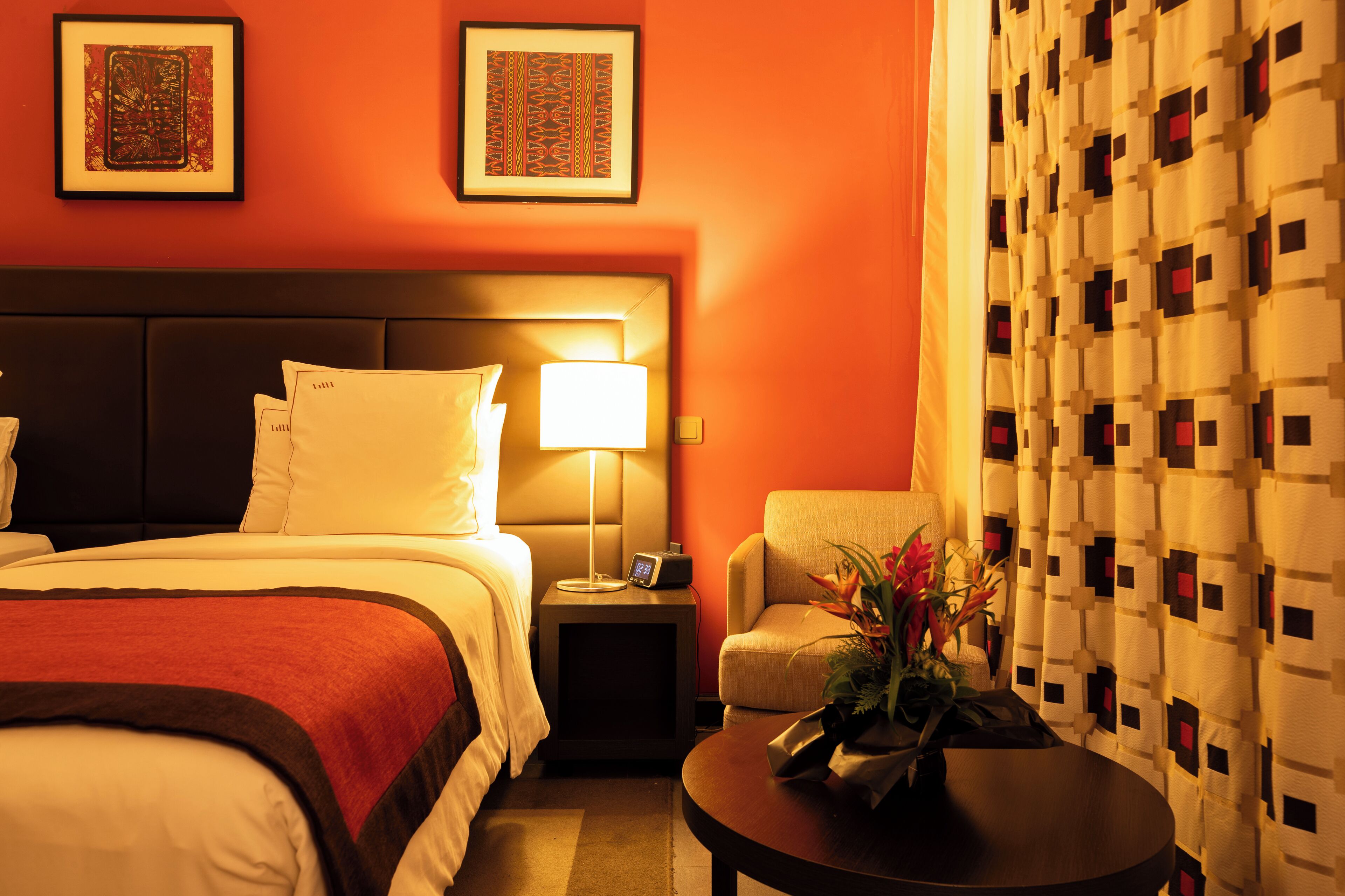 A hotel room with a bed, bedside table, lamp, chair, and a decorative vase.